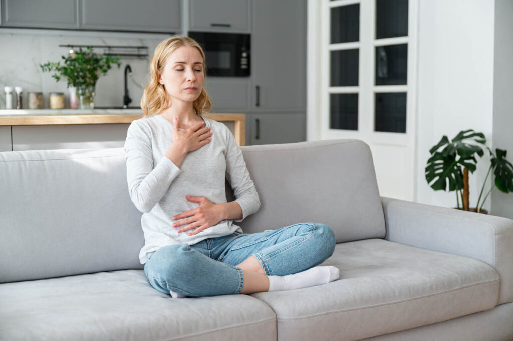 person sitting on comfortable couch doing deep breathing exercises after learning how to stay positive in difficult times