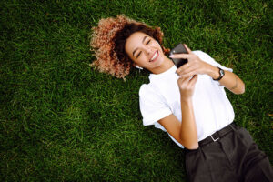 a person in a sober living program lies in the grass smiling at their phone
