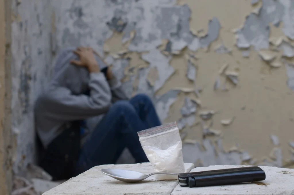 man sitting in a corner with head down in hands - drug dependency - heroin