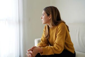 young woman seated on couch and staring calmly out window while practicing one of 5 effective strategies for anxiety